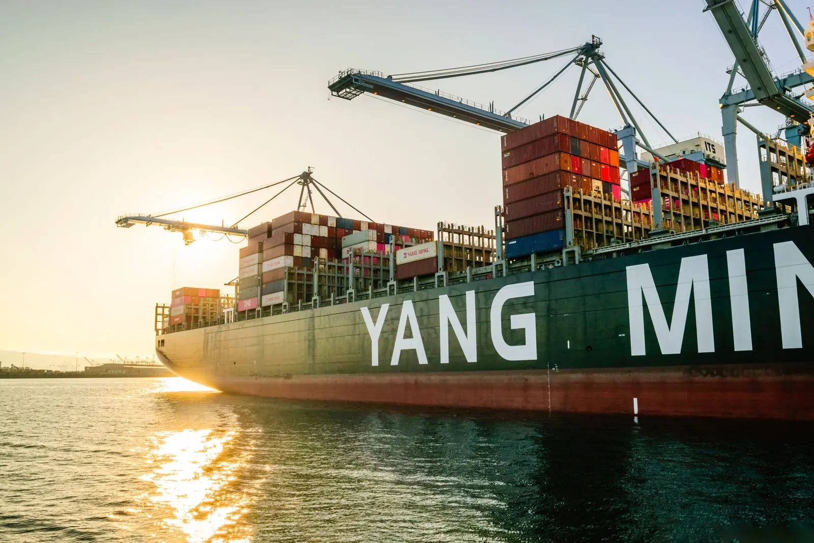 Illustrative photograph: A large cargo ship at a port in warm evening light.