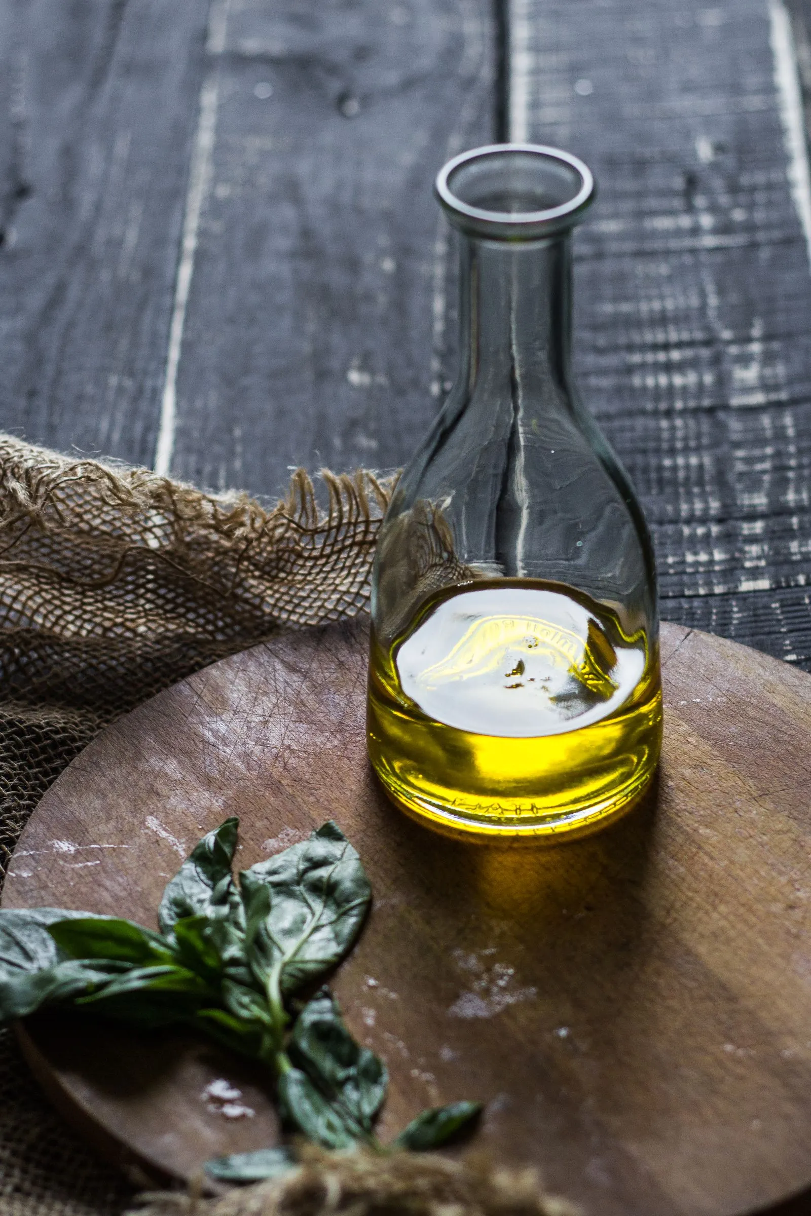 Illustrative photograph: A glass olive oil bottle with basil leaves on a wooden cutting board.