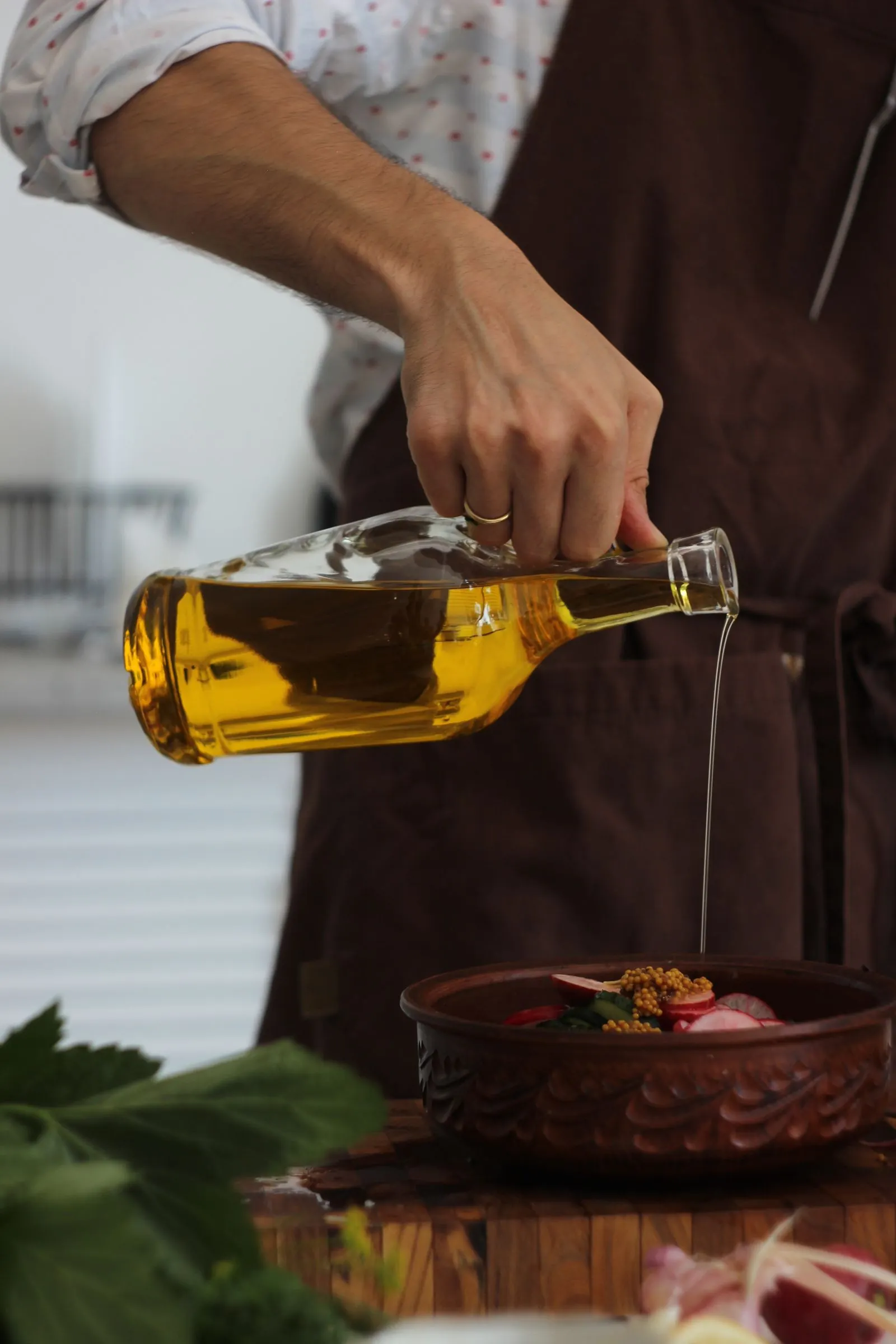 Une personne verse de l’huile d’olive depuis une bouteille sur des ingrédients frais