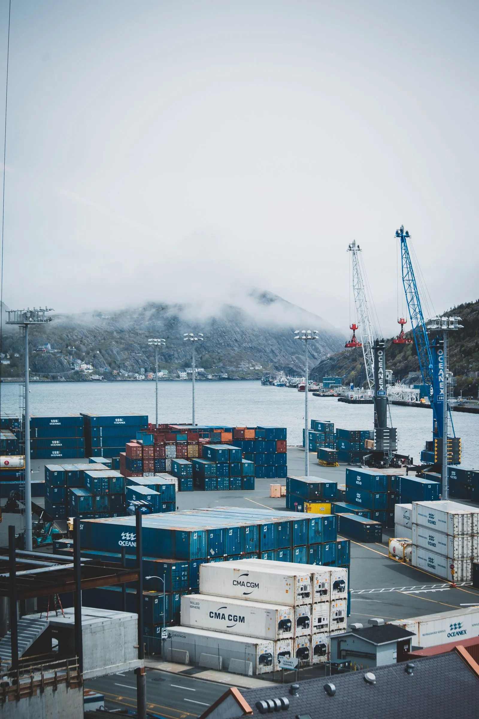 Contenedores de carga y grúas en un puerto junto al agua, entre la niebla.