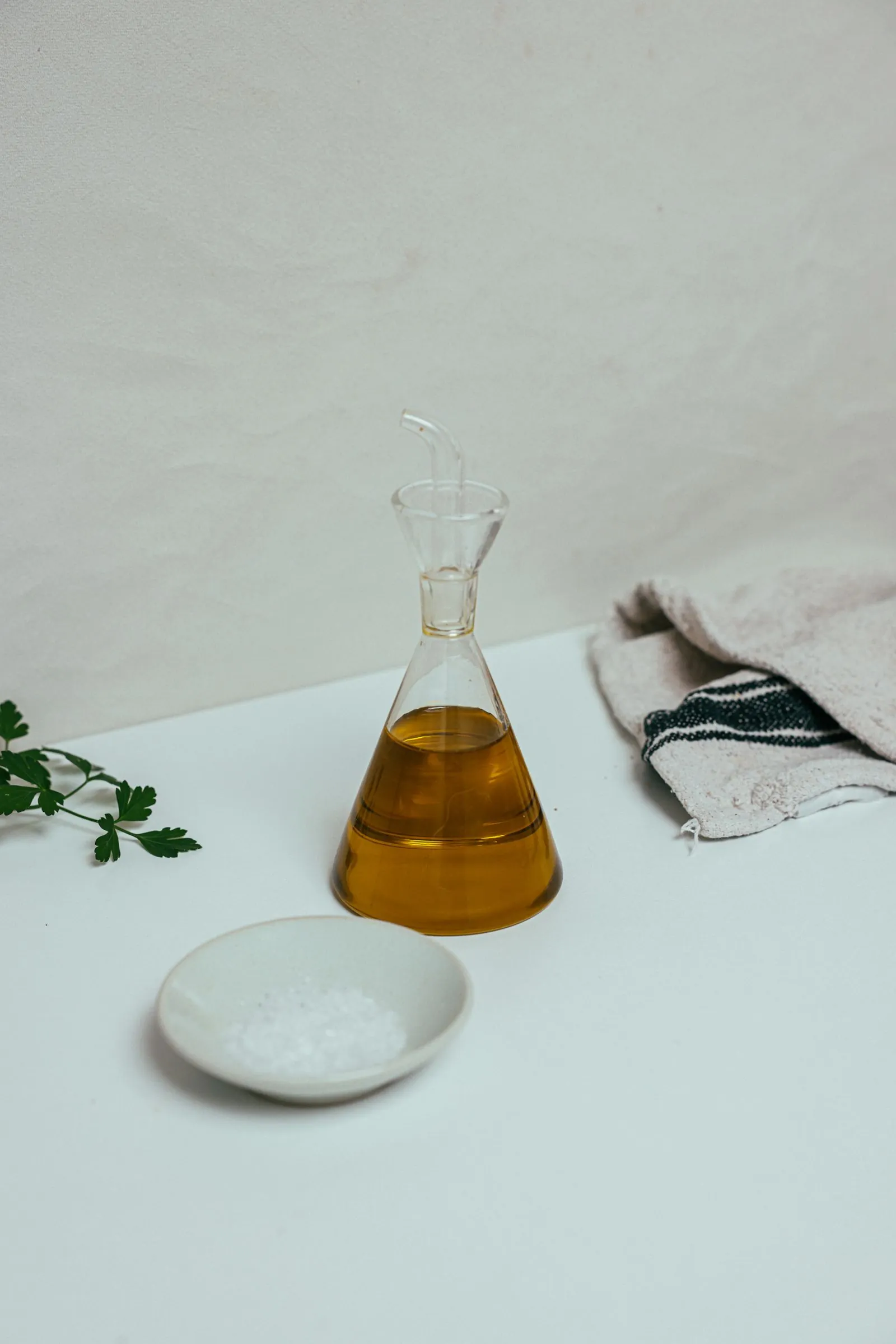 Illustrative photograph: A clear glass oil bottle beside a white saucer of salt on a light surface.