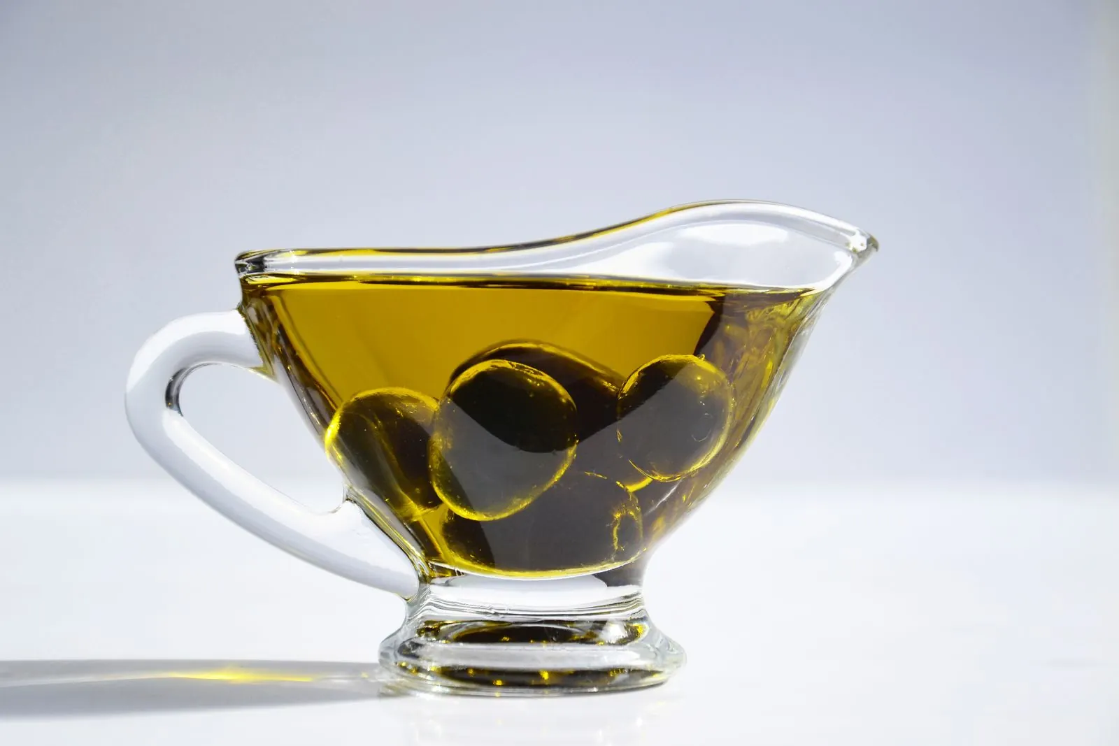 Illustrative photograph: Green olives rest across a glass cup filled with golden oil.