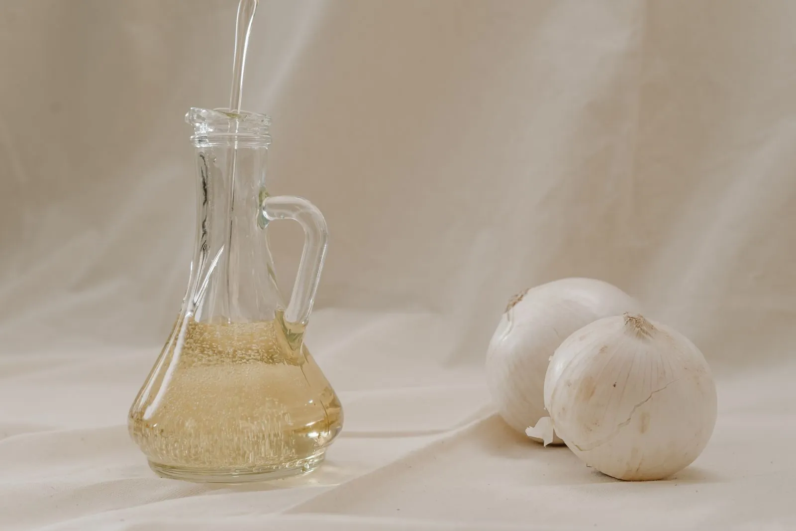 Illustrative photograph: Oil is poured into a clear jar beside garlic bulbs on a neutral surface.