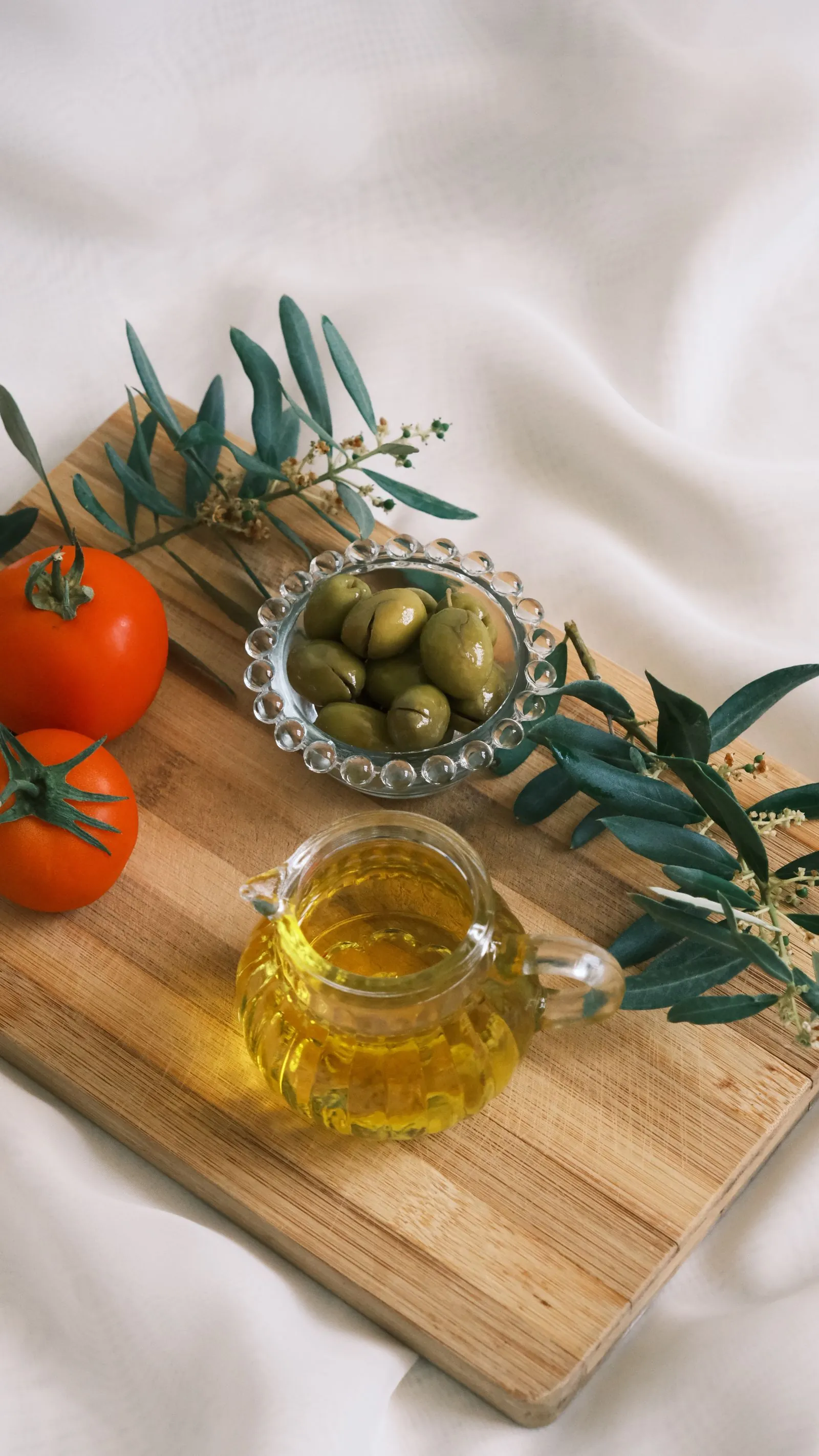 Illustrative photograph: Olive oil, green olives and tomatoes arranged on a wooden board.